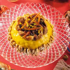 Pangialli ricetta: dolce giallo decorato con frutta secca e scorze d'arancia, circondato da noci su un piatto di cristallo.