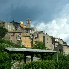 Antico borgo di **Tuscie Vetralla**, con case in pietra aggrappate alla collina sotto un cielo nuvoloso.