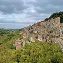 Case aggrappate alla roccia, un borgo pittoresco vicino al lago di Vico, con una valle verdeggiante.