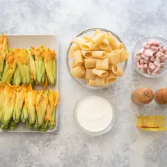 Fiori di zucca freschi, rigatoni, guanciale a cubetti, panna, sale, pepe e un pezzo di formaggio. Ingredienti per un piatto gustoso.