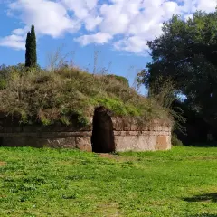 Antica tomba etrusca nel Lazio, con un ingresso ad arco e un tumulo ricoperto di vegetazione.