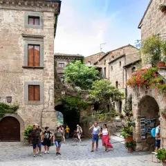 Un vicolo pittoresco nella Tuscia, con case in pietra, fiori colorati e turisti che passeggiano.