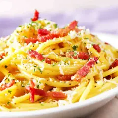 Un piatto fumante di spaghetti alla carbonara, uno dei secondi piatti tipici del Lazio, con guanciale croccante, pecorino romano e prezzemolo tritato.