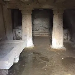 Interno di una tomba a dado scavata nella roccia, con un sarcofago in pietra e colonne grezze.