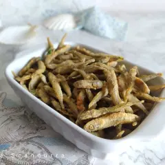Un piatto bianco pieno di lattarini pesce fritti, croccanti e dorati, con un tocco di prezzemolo.