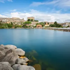 Vista del lago di Bolsena con il borgo in lontananza. Il diametro del lago di Bolsena è imponente, con acque calme e rocce in primo piano.