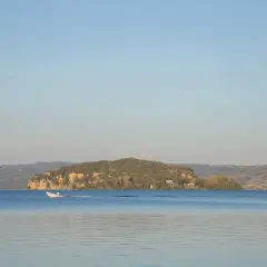 Un'isola Martana verdeggiante si staglia sul lago azzurro, con una barca bianca che solca le acque calme.