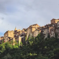 Antiche case in pietra si aggrappano alla collina a Capranica, Viterbo, con vegetazione lussureggiante che le circonda.