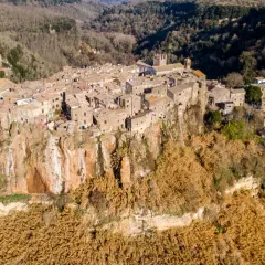 Antico borgo di Calcata Viterbo arroccato su una rupe tufacea, circondato da vegetazione secca e boschi.