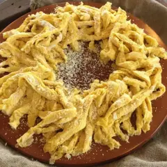 Frittelloni di Civita Castellana, pasta fresca fatta in casa, cosparsa di formaggio grattugiato, disposta a corona su un piatto di terracotta.