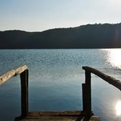 Un pontile in legno si affaccia sul lago di Mezzano, con il sole che brilla sull'acqua e le colline sullo sfondo.