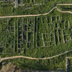 Vista aerea della necropoli centocamere, con rovine antiche immerse nel verde e sentieri che le attraversano.