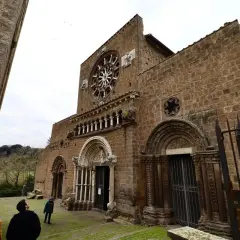 La facciata romanica di Santa Maria Maggiore a Tuscania, con il suo rosone e i portali scolpiti, vista da un angolo con visitatori che ammirano la struttura.