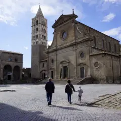 Una famiglia passeggia nella storica piazza San Lorenzo a Viterbo, ammirando la maestosa cattedrale e il suo campanile.