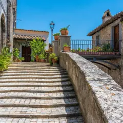 Scalinata acciottolata a Castiglione in Teverina, con vasi di fiori e case in pietra sotto un cielo azzurro.