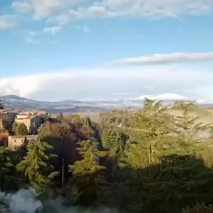 Borgo medievale con torre imponente, immerso nel verde del comune di Proceno, con colline nebbiose all'orizzonte.