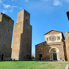 Le chiese di Tuscania, con le loro torri medievali e la facciata romanica, si stagliano contro un cielo azzurro.