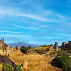 Paesaggio collinare con rovine di castelli e chiese, sotto un cielo azzurro. Un luogo che evoca la storia della riserva naturale di Tuscania.