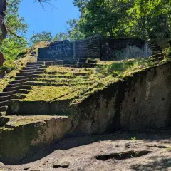 Antica piramide etrusca scavata nella roccia, ricoperta di muschio e circondata da alberi secolari.