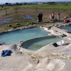 Persone si rilassano nelle acque termali del lago Viterbo, con un paesaggio rurale sullo sfondo.