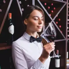 Sommelier annusa un bicchiere di vino Cannaiola, circondata da scaffali pieni di bottiglie.