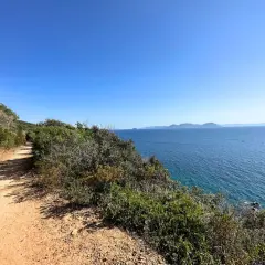 Sentiero sabbioso nella selva del Lamone, con vista sul mare blu e isole all'orizzonte.