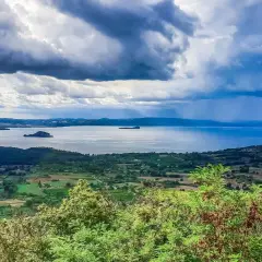 Vista panoramica del lago di Bolsena con isole, colline verdi e un cielo drammatico. Un paesaggio mozzafiato da Capodimonte.