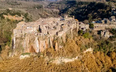 Antico borgo di Calcata Viterbo arroccato su una rupe tufacea, circondato da vegetazione secca e boschi.