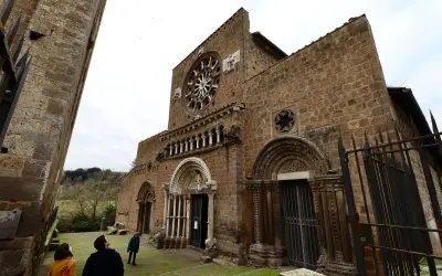 La facciata romanica di Santa Maria Maggiore a Tuscania, con il suo rosone e i portali scolpiti, vista da un angolo con visitatori che ammirano la struttura.
