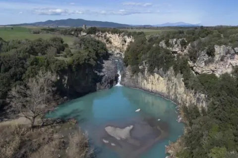 Cascata del Pelago, un gioiello naturale dove si trova Vulci, con acque turchesi che si infrangono tra rocce e vegetazione lussureggiante.