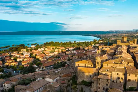 Borghi da visitare vicino Bolsena: vista aerea di un antico castello e case con tetti in tegole rosse, con il lago sullo sfondo.