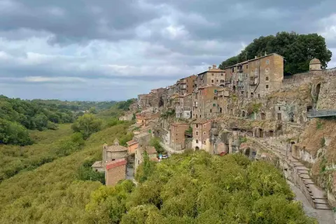 Case aggrappate alla roccia, un borgo pittoresco vicino al lago di Vico, con una valle verdeggiante.