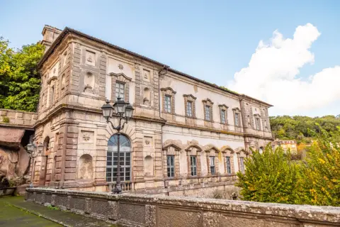 Il **Palazzo Chigi Soriano nel Cimino**, con la sua facciata imponente e le finestre eleganti, si staglia contro un cielo azzurro con nuvole bianche.