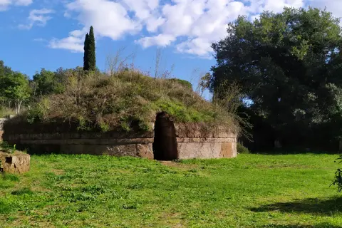 Antica tomba etrusca nel Lazio, con un ingresso ad arco e un tumulo ricoperto di vegetazione.