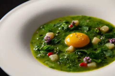 Un piatto verde brillante con un tuorlo d'uovo dorato, erbe fresche e fiori viola, un'interpretazione moderna dei piatti tipici viterbesi.
