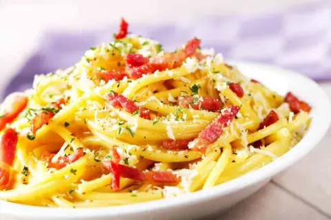 Un piatto fumante di spaghetti alla carbonara, uno dei secondi piatti tipici del Lazio, con guanciale croccante, pecorino romano e prezzemolo tritato.
