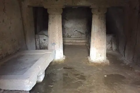 Interno di una tomba a dado scavata nella roccia, con un sarcofago in pietra e colonne grezze.