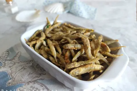 Un piatto bianco pieno di lattarini pesce fritti, croccanti e dorati, con un tocco di prezzemolo.