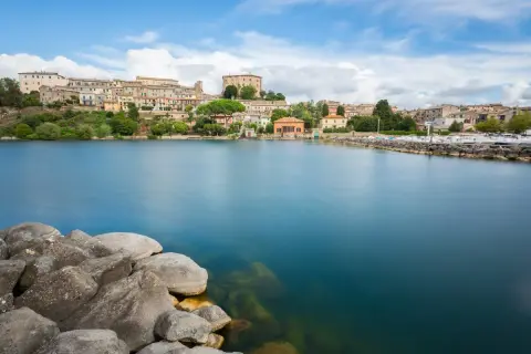Vista del lago di Bolsena con il borgo in lontananza. Il diametro del lago di Bolsena è imponente, con acque calme e rocce in primo piano.