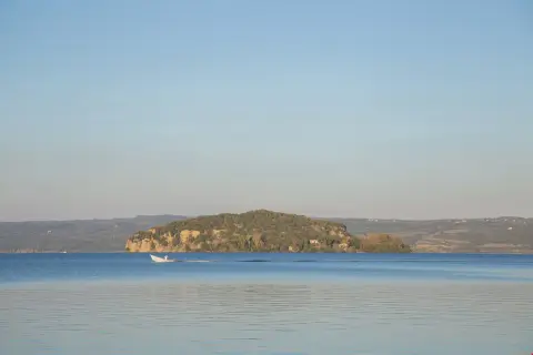 Un'isola Martana verdeggiante si staglia sul lago azzurro, con una barca bianca che solca le acque calme.