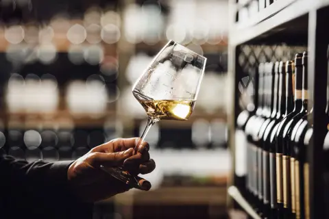 Un calice di vino Grechetto, con le sue caratteristiche note dorate, in una cantina con bottiglie sullo sfondo.