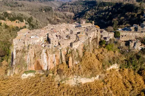 Antico borgo di Calcata Viterbo arroccato su una rupe tufacea, circondato da vegetazione secca e boschi.