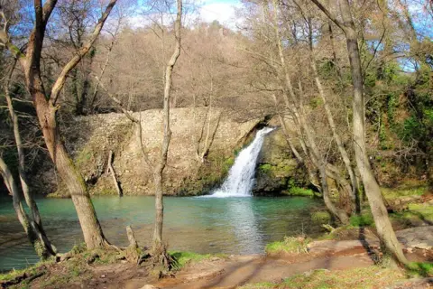 Cascata della mola di Oriolo, con acque turchesi e alberi spogli che incorniciano la scena.