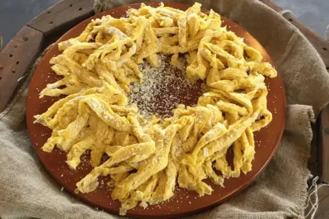 Frittelloni di Civita Castellana, pasta fresca fatta in casa, cosparsa di formaggio grattugiato, disposta a corona su un piatto di terracotta.