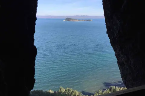 Vista da una grotta sul lago, con un'isola verde in lontananza. Il **monte Bisenzio** si staglia all'orizzonte.