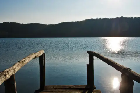 Un pontile in legno si affaccia sul lago di Mezzano, con il sole che brilla sull'acqua e le colline sullo sfondo.