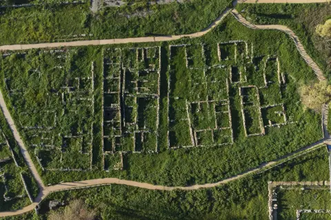 Vista aerea della necropoli centocamere, con rovine antiche immerse nel verde e sentieri che le attraversano.