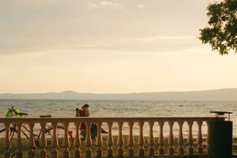 Tramonto sulle spiagge del lago di Bolsena. Una persona in sedia a sdraio, biciclette e un albero creano un'atmosfera serena.