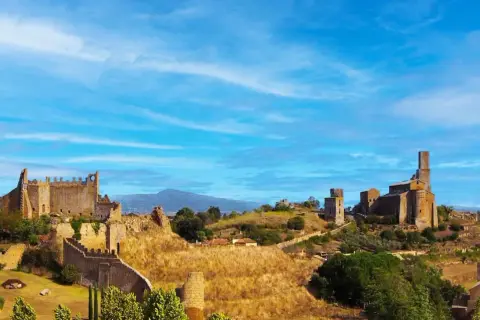 Paesaggio collinare con rovine di castelli e chiese, sotto un cielo azzurro. Un luogo che evoca la storia della riserva naturale di Tuscania.