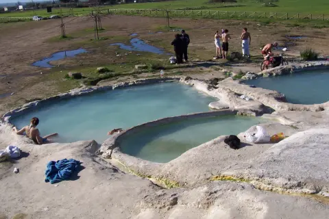 Persone si rilassano nelle acque termali del lago Viterbo, con un paesaggio rurale sullo sfondo.
